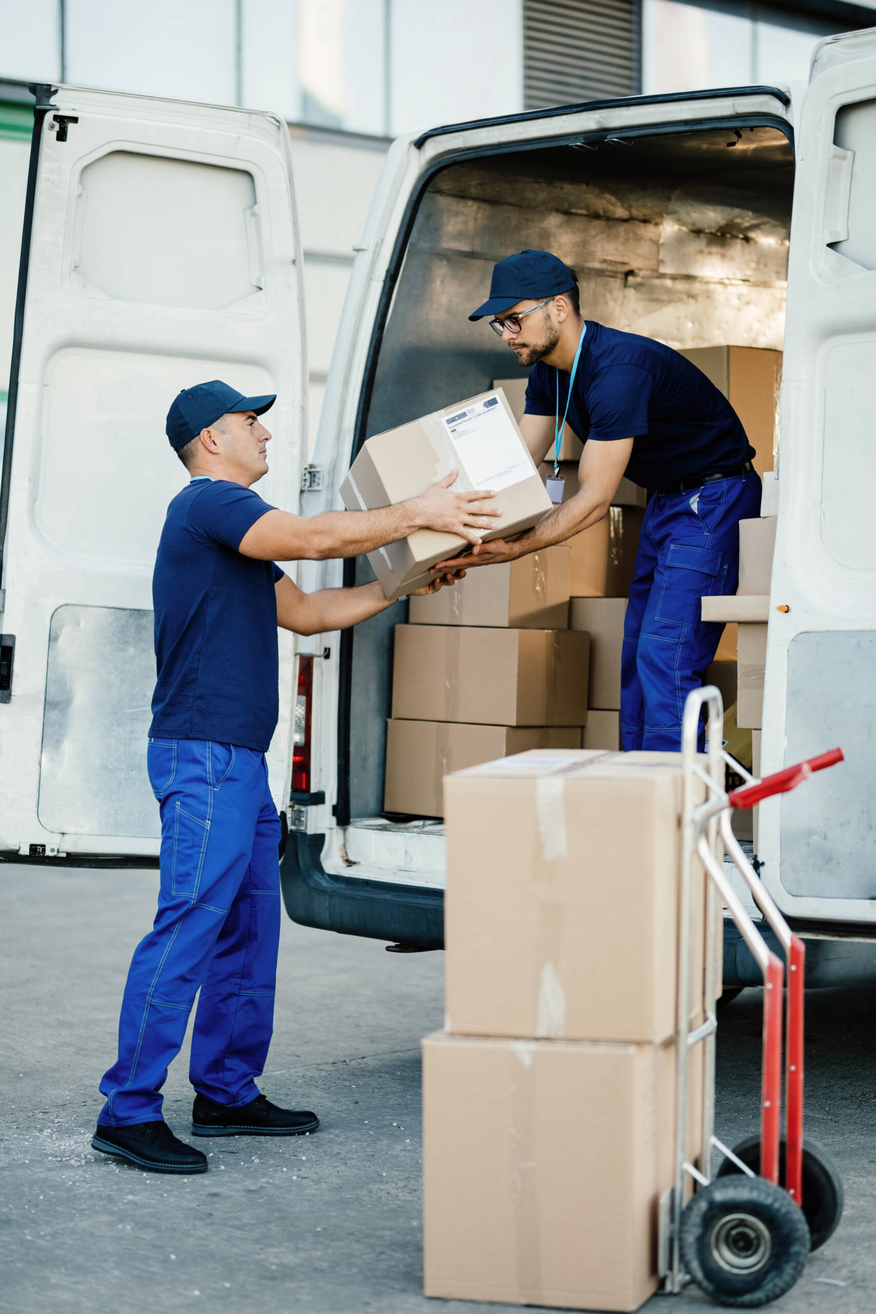 Male workers cooperating while loading cardboard boxes in a delivery van.